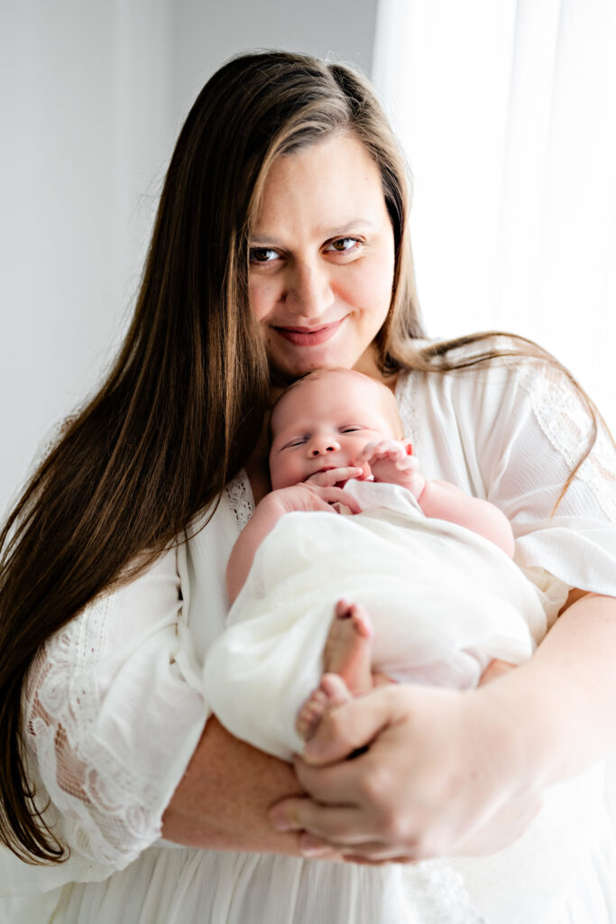A mother smiles at the camera while holding her newborn daughter