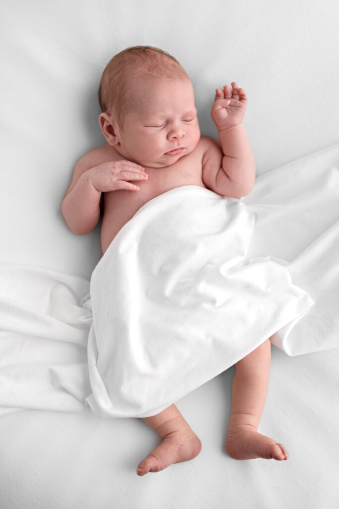 Newborn baby girl swaddled in a white blanket and sleeps during her newborn photoshoot