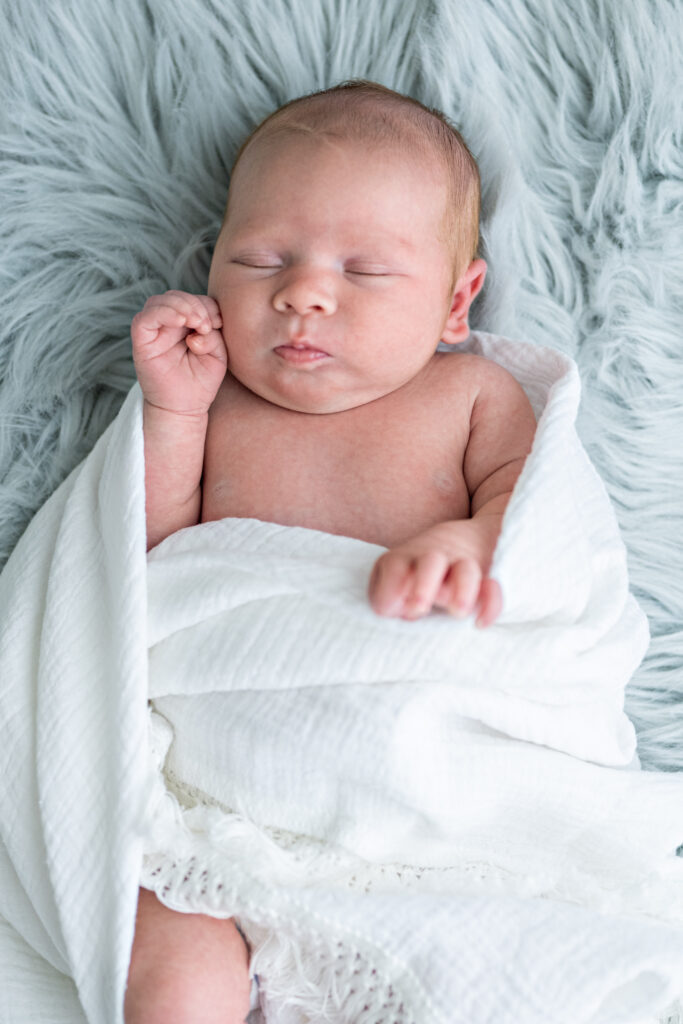 A newborn baby sleeps on a soft blue carpet during a newborn photoshoot