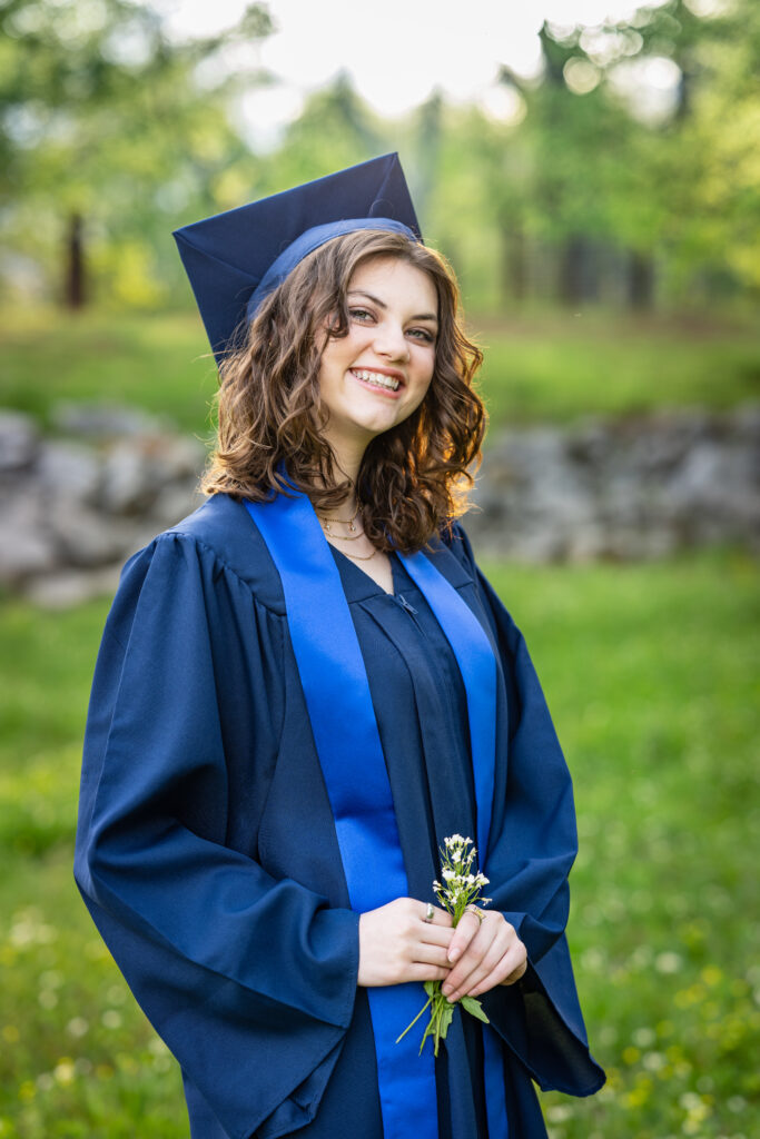 Senior girl smiles for the camera dressed in her cap and gown at Hayes Nature Preserve in Huntsville, Alabama