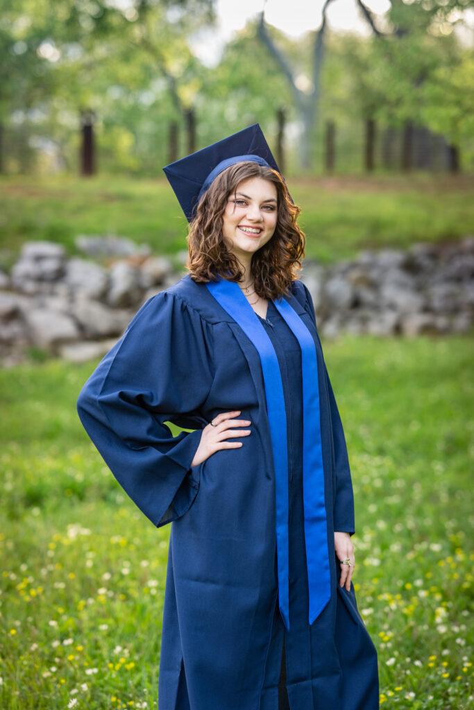 Senior girl poses for the camera dressed in her cap and gown at Hayes Nature Preserve in Huntsville, Alabama