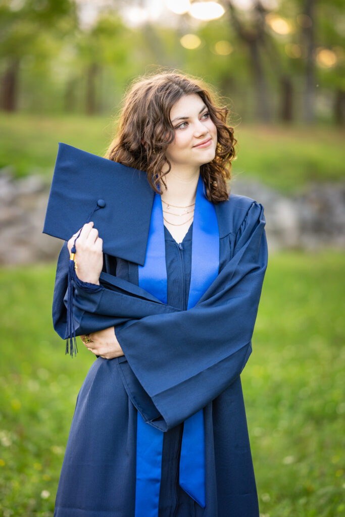 Senior girl poses for the camera dressed in her cap and gown at Hayes Nature Preserve in Huntsville, Alabama