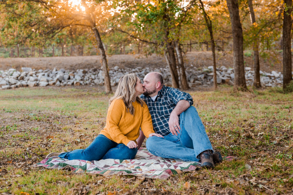 A couple sitting on the ground and kissing as the sun sets behind them at Hayes Nature Preserve in Huntsville Alabama