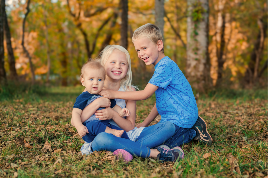 Siblings sit in the grass and play together during pictures at Hayes Nature Preserve in Huntsville Alabama