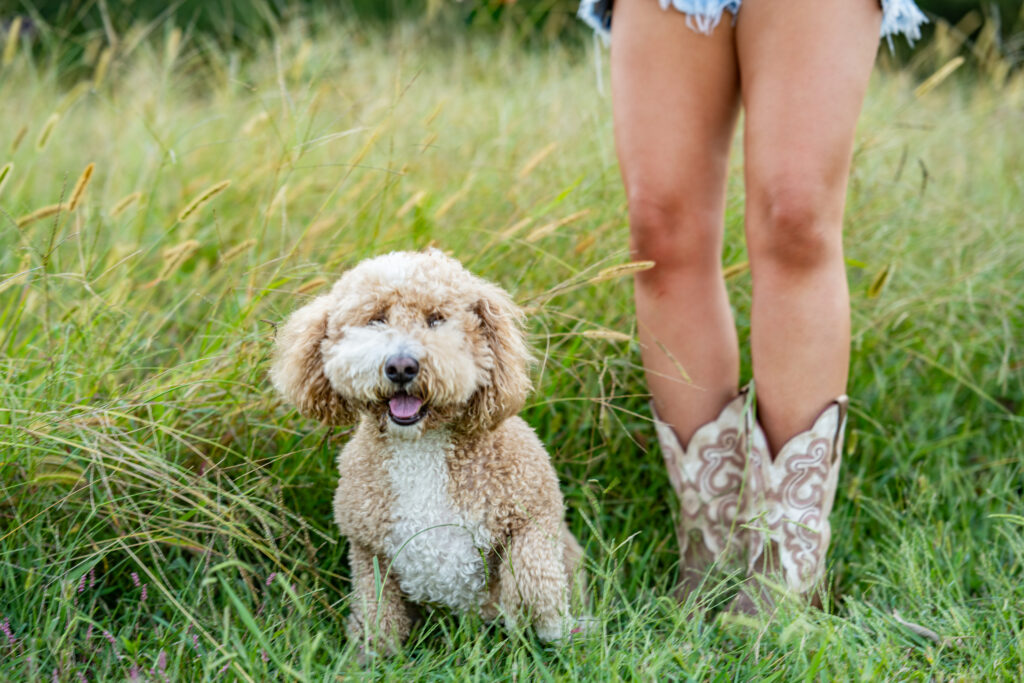 A senior girl standing in her boots with her dog sitting next to her at Hays Nature Preserve